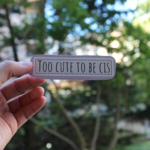 Photo d'un stickers. Il est écrit "Too cute to be cis" en noir, avec un cadre pointillé rose et bleu.