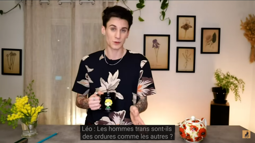 Capure d'écran de la vidéo de Léo, un homme blanc avec des tatouages et une un T-shirt à fleur. Il dit : « Les hommes trans sont-ils des ordures comme les autres ? » 