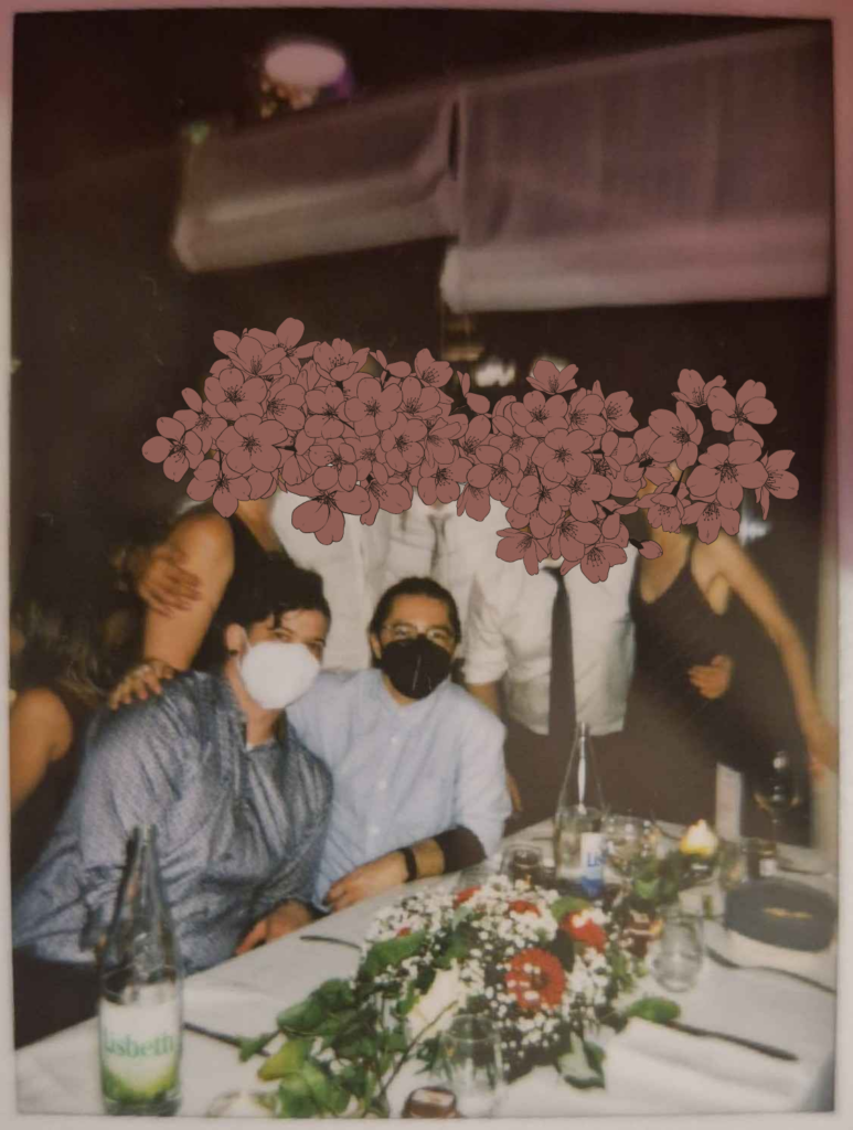 Photo polaroid d'un groupe de personnes posant pour la photo. Quatre d'entre-elles sont debout et leurs visages on été censurés par des dessins de fleurs. Deux sont assis devant elles, moi et mon partenaire, deux hommes blancs en chemise bleue. Je porte un masque FFP2 noir et mon partenaire un blanc.